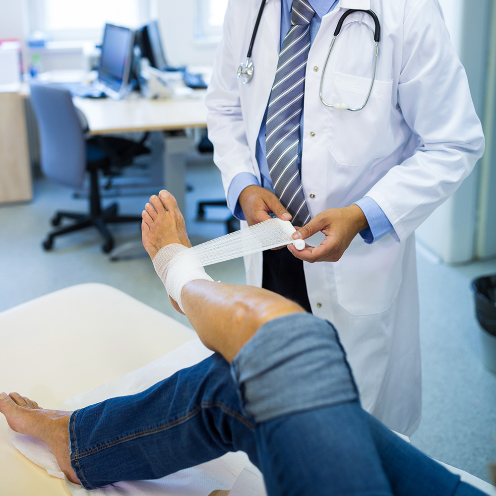 Male doctor bandaging foot of female patient in hospital